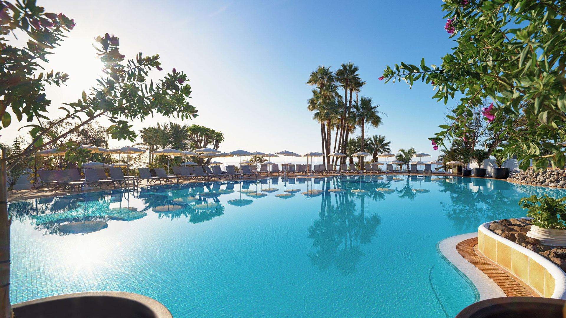 Großzügiger Poolbereich des Hotel Jardín Tecina bei Playa de Santiago mit Liegen, Sonnenschirmen und Palmenkulisse.