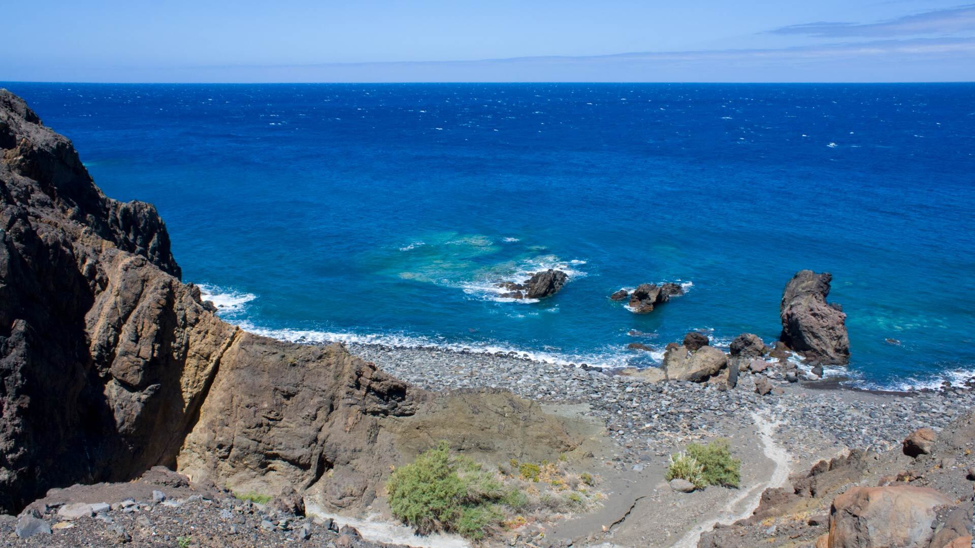 An der Playa del Trigo auf leuchtet das Meer in kräftigem Blau vor der schroffen Felsküste.