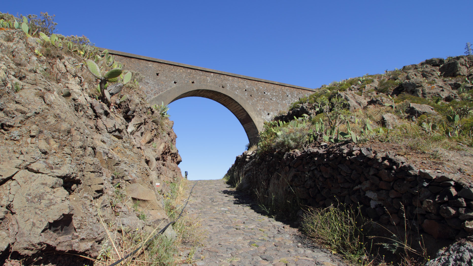 Historisches Aquädukt überspannt den gepflasterten GR 132 zwischen Kakteen und Trockenmauern beim Mirador Ermita del Santo.