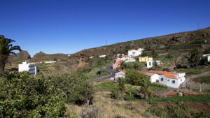 Blick auf das Hochlanddorf Arure mit seinen farbenfrohen Häusern, Palmen und der kurvigen Zufahrtsstraße durch das karge Hochland.