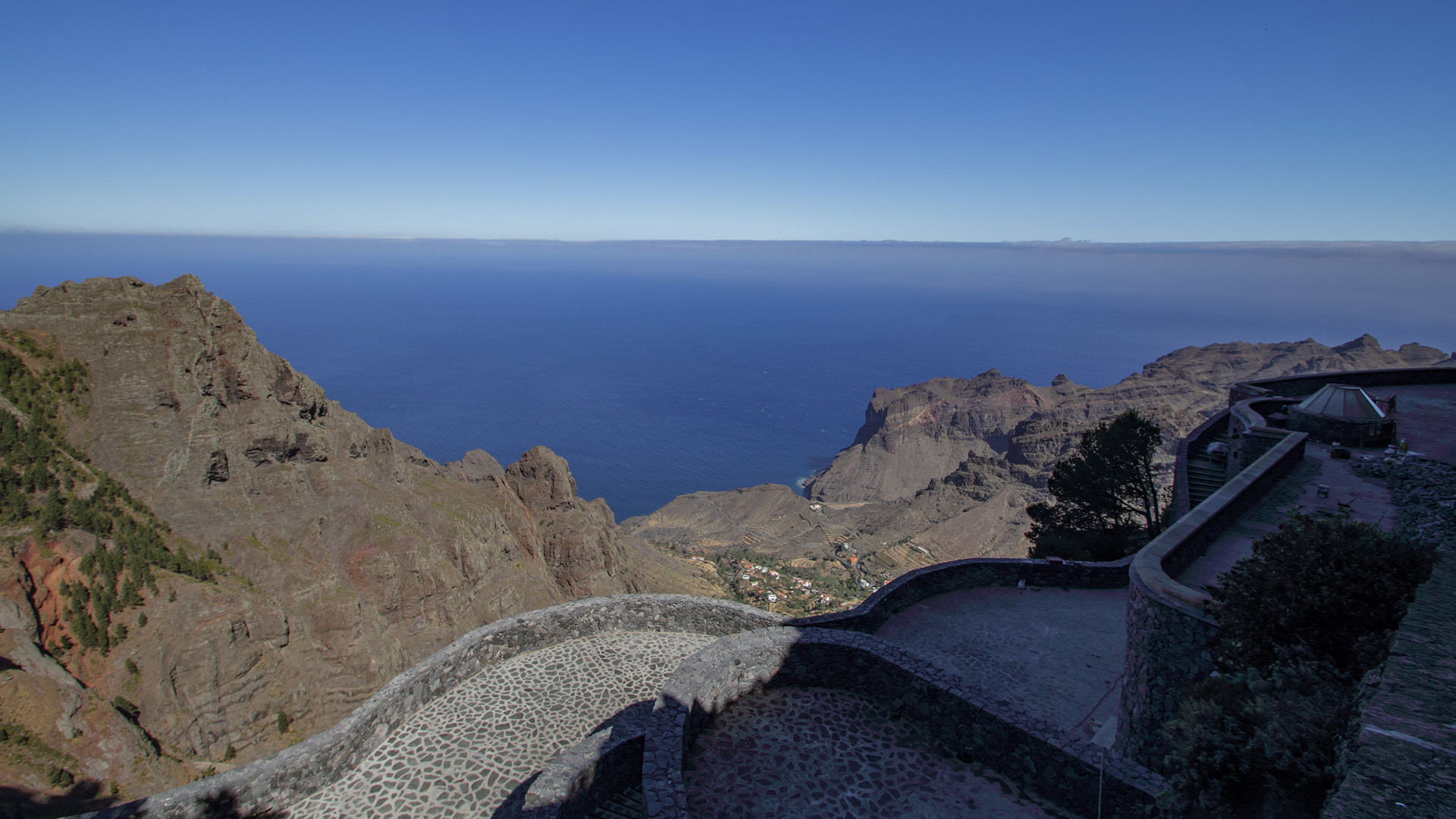Blick über die geschwungene, gemauerte Aussichtsplattform des Mirador Ermita del Santo auf Berge, Küste und Atlantik.