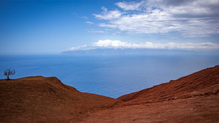 hinter den leuchtend roten Erosionsflächen des Mirador de Abrante erhebt sich Teneriffa am Horizont